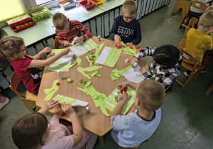 Dzieci przyklejają kawałki papieru tworząc trawę.