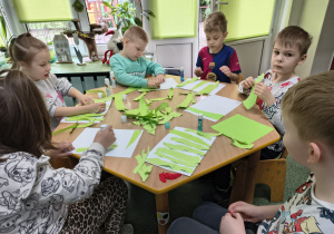 Dzieci przyklejają kawałki papieru tworząc trawę.