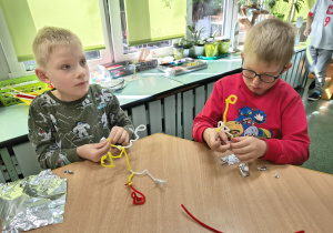 Chłopcy tworzą rzeźby z kolorowych drucików kreatywnych i oplatają je folią aluminiową.