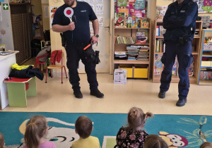 Umundurowany policjant prezentuje okrągły, biały znak z czerwonym środkiem.