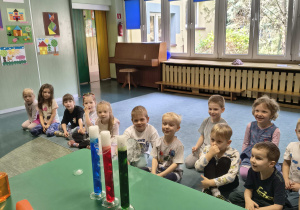 Dzieci obserwują trzy menzurki z kolorową wodą, z dodanym suchym lodem. Lód na końcu każdej z nich wydziela parę.