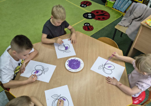 Dzieci nakładają rosnącą farbę na śliwkę.