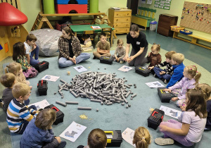 Dzieci siedzą w kręgu i słuchają instrukcji budowania.