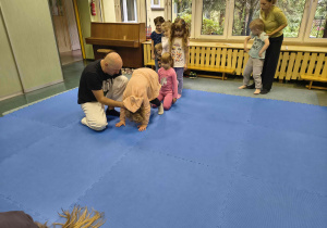 Dzieci wykonują przewrót w przód z pomocą instruktora.