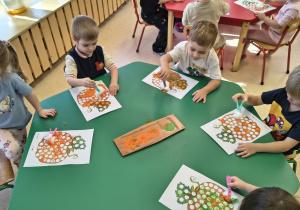 Dzieci stemplują farbami dynię.