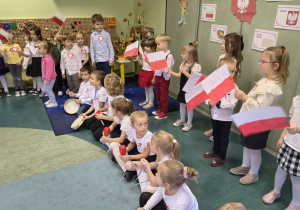 Dzieci śpiewają posenkę trzymając w ręku flagę Polski.