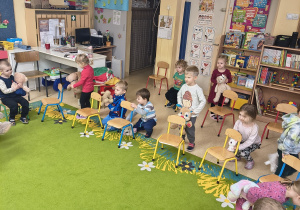 Dzieci układają swoje misie w różnych pozycjach względem krzesła.