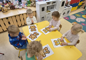 Dzieci zapełniają plasteliną kontury białych kółek.