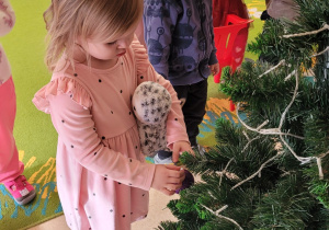 Dziewczynka zakłada bombkę na choinkę.