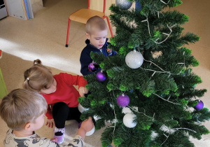 Dziweci zakładają kolorowe bombki na choinkę.