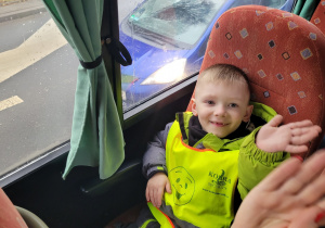 Chłopiec z grupy Motylków uśmiecha się i macha do nauczyciela.