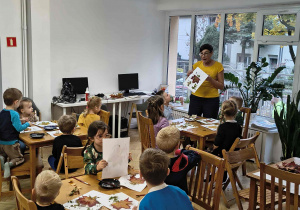 Dzieci przy stolikach tworzą jesienne prace plastyczne z wykorzystaniem materiałów przyrodniczych.