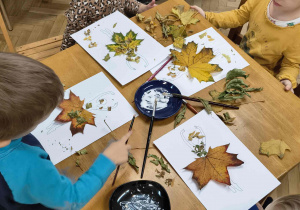 Dzieci przyklejają suche liście do kartki.