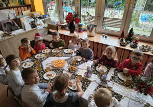 Grupa dzieci siedzi przy wigilijnym stole.