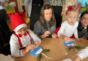 Dziewczynka i chłopiec ozdabiają bombki wraz z rodzicami.