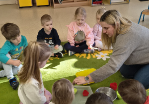 Dzieci obserwują jak nauczycielka napełnia wodą foremki za pomocą pipetki.
