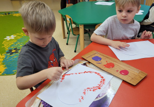Chłopiec tworzy serduszko za pomocą patyczków i farby.