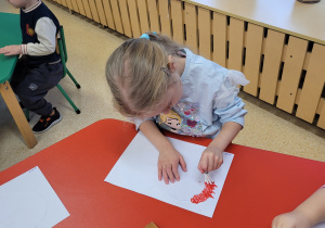 Dziewczynka odciska patyczki zanurzone w farbie.