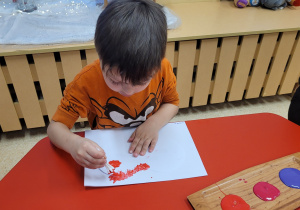 Chłopiec stempluje za pomocą patyczków.