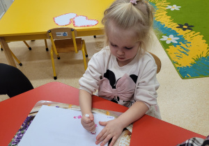 Dziewczynka wykonuje serduszko za pomocą farby.