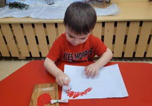 Chlopiec stempluje za pomocą farby i patyczków kosmetycznych.