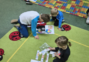 Dzieci siedzą na dywanie i układają w całość zdjęcie misia.