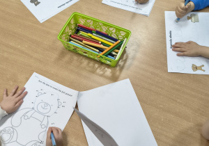Przedszkolaki wykonują przy stoliku kartę pracy o misiu.