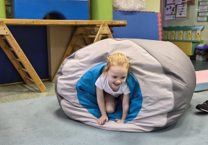 Dziewczynka przeciska się przez tunel gimnastyczny.