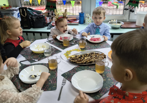 Przedszkolaki świętują przy stole jedząc wigilijny obiad.
