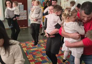 Rodzice trzymają dzieci na rękach w zabawie tanecznej.