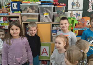 Dzieci stoją przy szafce, na której jest naklejona samogłoska A.