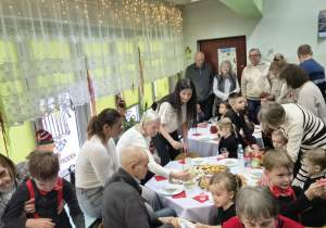 Dziadkowie z wnukami siedzą przy stole podczas poczętunku.