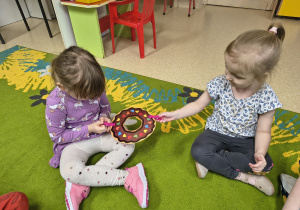 Dziewczynki przekazują sobie papierowego pączka za pomocą klamerek.