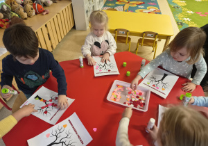 Dzieci przyklejają papierowe serduszka na drzewko.