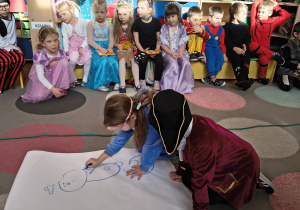 Dzieci rysują wspólnie bałwanka mając zasłonięte oczy.