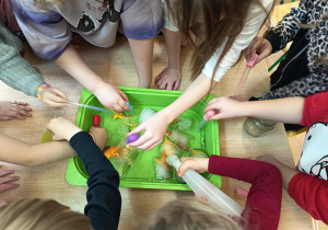 Dzieci próbują wydobyć figurki dinozaurów z lodu.