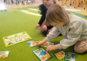 Dziewczynka układa dinozaurowe puzzle.