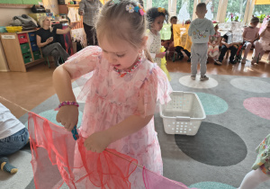 Dziewczynka rozkłada kolorową chustę na sznurku.