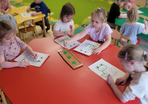Dzieci malują zieloną farbą żabki.
