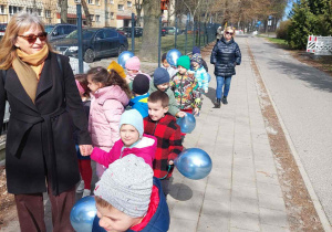Dzieci spacerują z niebieskimi balonami na znak solidaryzmu z osobami z autyzmem.