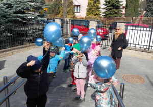 Dzieci świętują Światowy Dzień Autyzmu z niebieskimi balonami przed przedszkolem.
