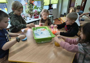 Dzieci malują farbą różne wzory na śniegu.