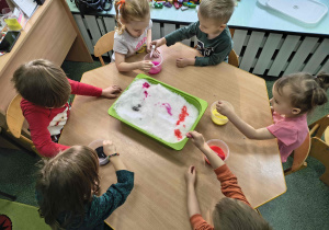 Dzieci malują kolorową farbą na śniegu.