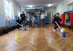 Dzieci wykonują slalom między pachołkami z dmuchanymi piłkami.