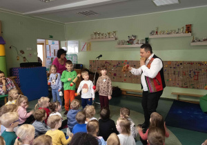 Dzieci trzymają małe instrumenty perkusyjne i naśladują ruchy prowadzącego.