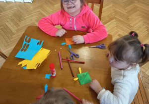Dzieci używają kolorowego papieru, nożyczek i kleju do tworzenia figurek zwierząt.