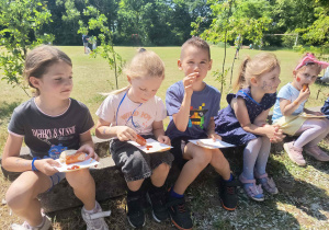Dzieci zjadają na pikniku pieczone kiełbaski.
