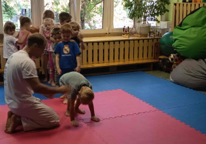 Instruktor asekuruje chłopca wykonującego przewrót.