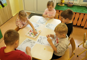 Dzieci ozdabiają plasteliną kropkę.