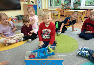 Dzieci biorące udział w zajęciach edukacyjnych, podczas których używają wagi szalkowej do ważenia owoców.